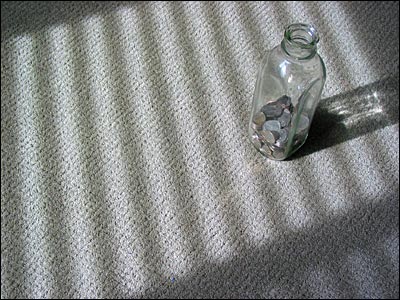 A milk bottle filled with coins sitting on the floor. Calgary. 16 March 2002. Copyright © 2002 Grant Hutchinson