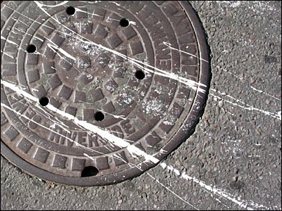 Paint spattered manhole. 5th Avenue Southwest, Calgary. 09 August 2002. Copyright © 2002 Grant Hutchinson